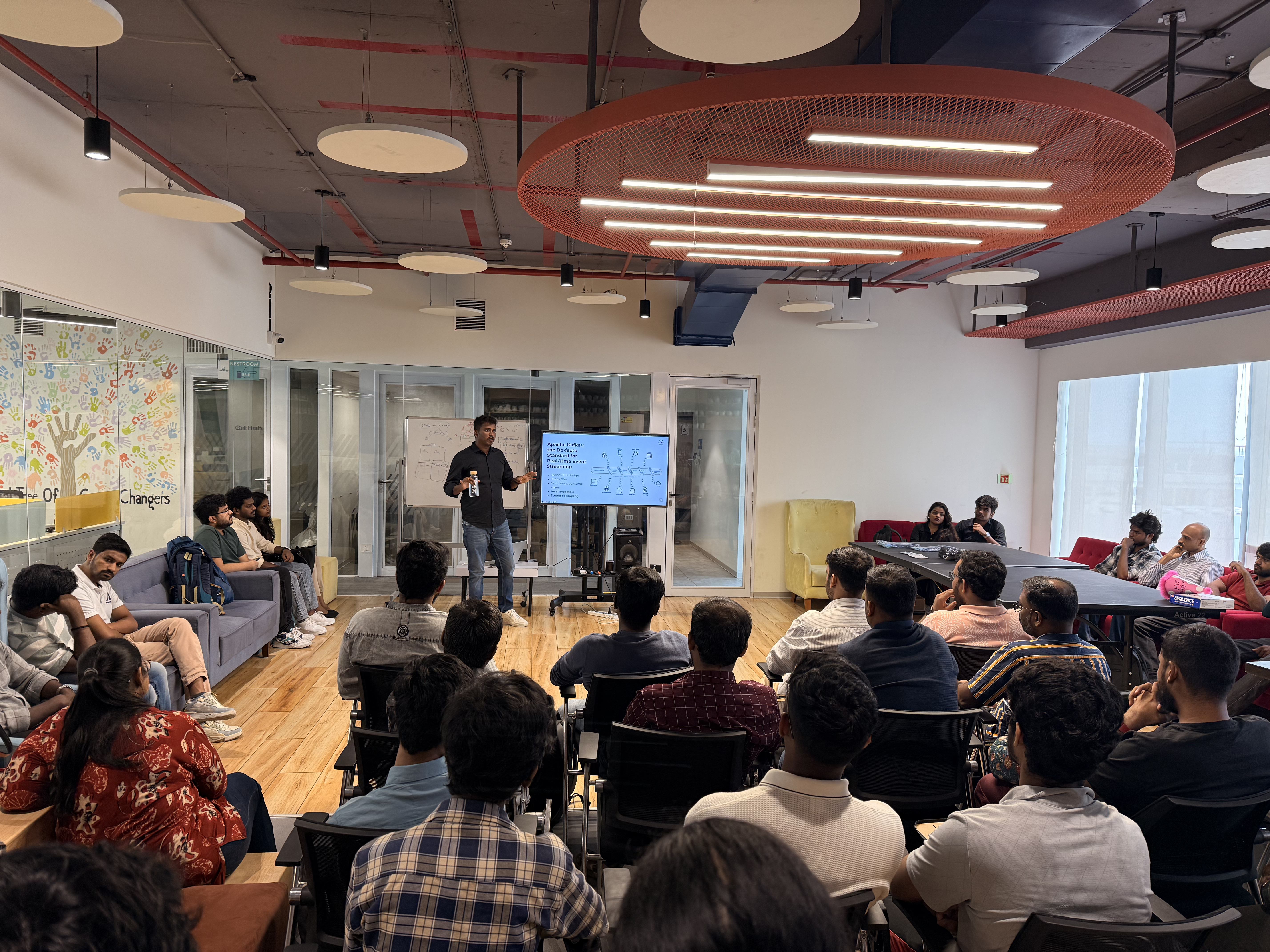 Mani Selvan presenting to a seated audience, a Kafka slide on screen