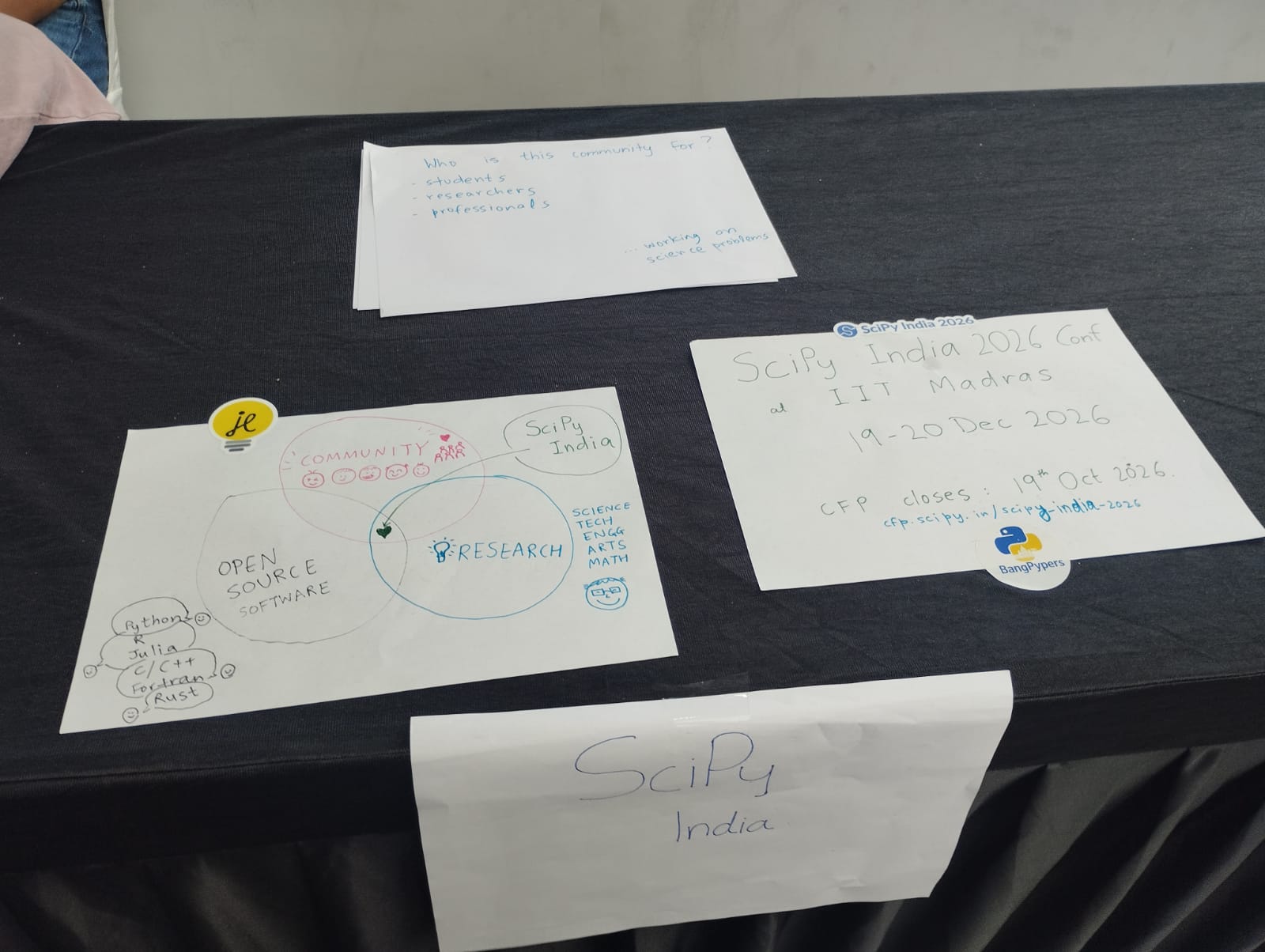 Handwritten SciPy India signs on the booth table, including one announcing SciPy India 2026 at IIT Madras on 19 and 20 December with the CFP closing on 19 October