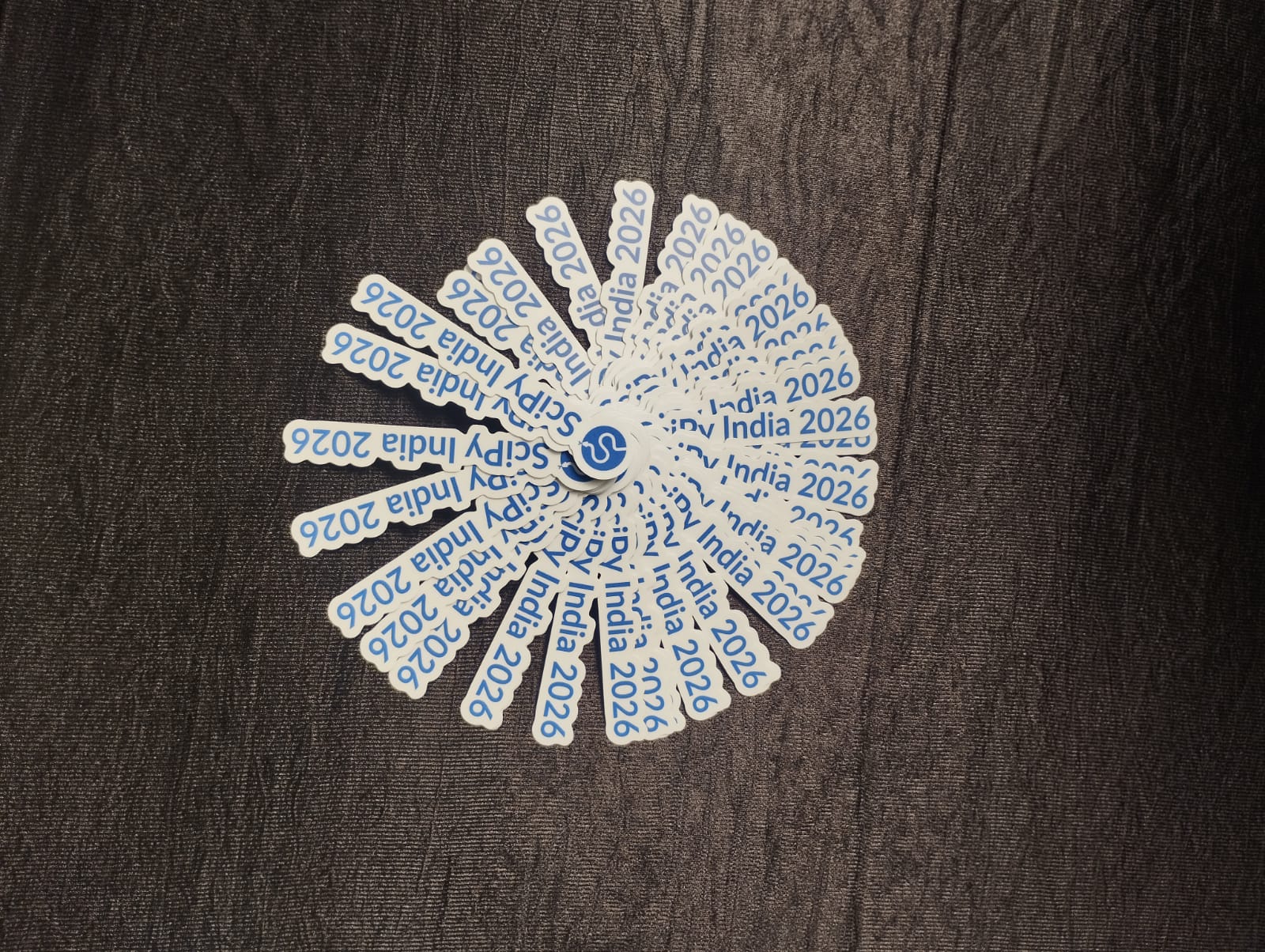 A fan of SciPy India 2026 stickers laid out on a dark table